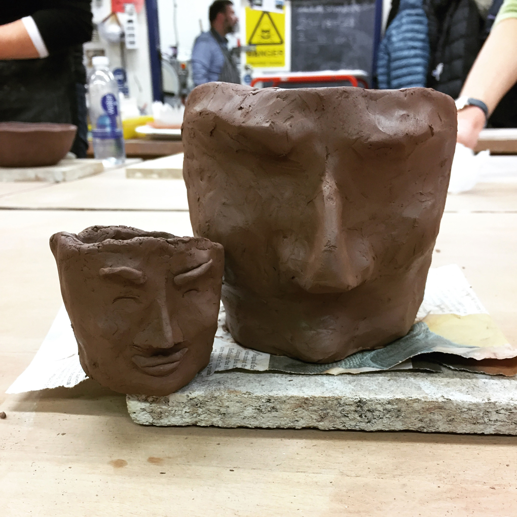Two unfired clay pots with partially-sculpted human faces on them