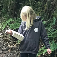 girl reading a book while walking through a wood