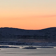 Sunrise over a flat landscape of snow and lakes with small mountains in the distance
