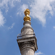 The Monument to the Great Fire of London rises above narrow London streets with its golden urn high up catching the sunlight.