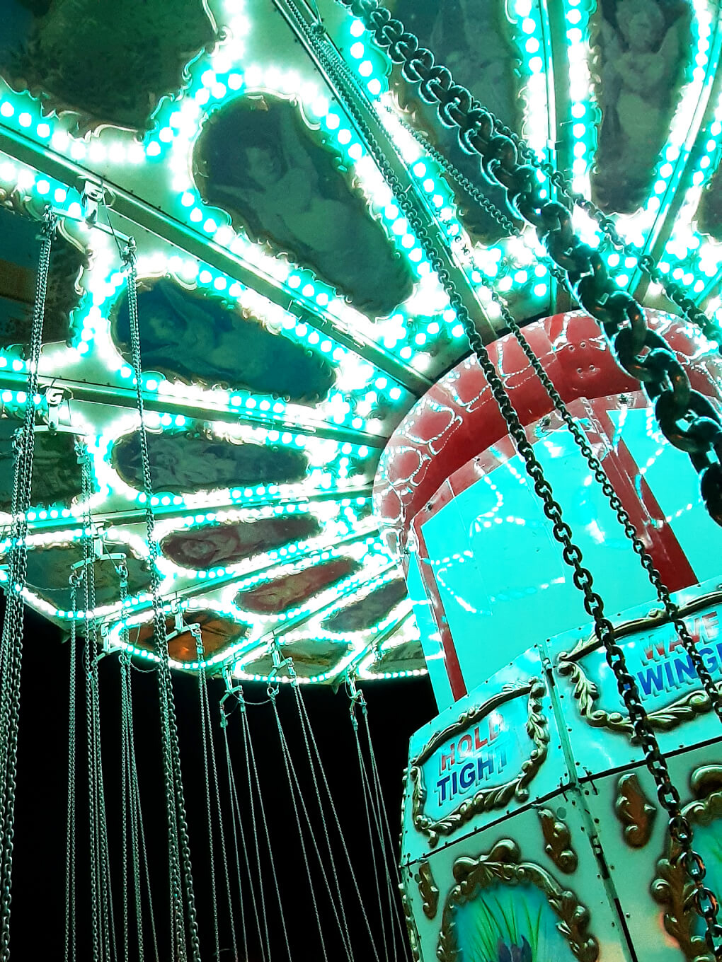 Bright lights in the canopy over a rotating swing ride, with chains to each seat hanging down into the picture
