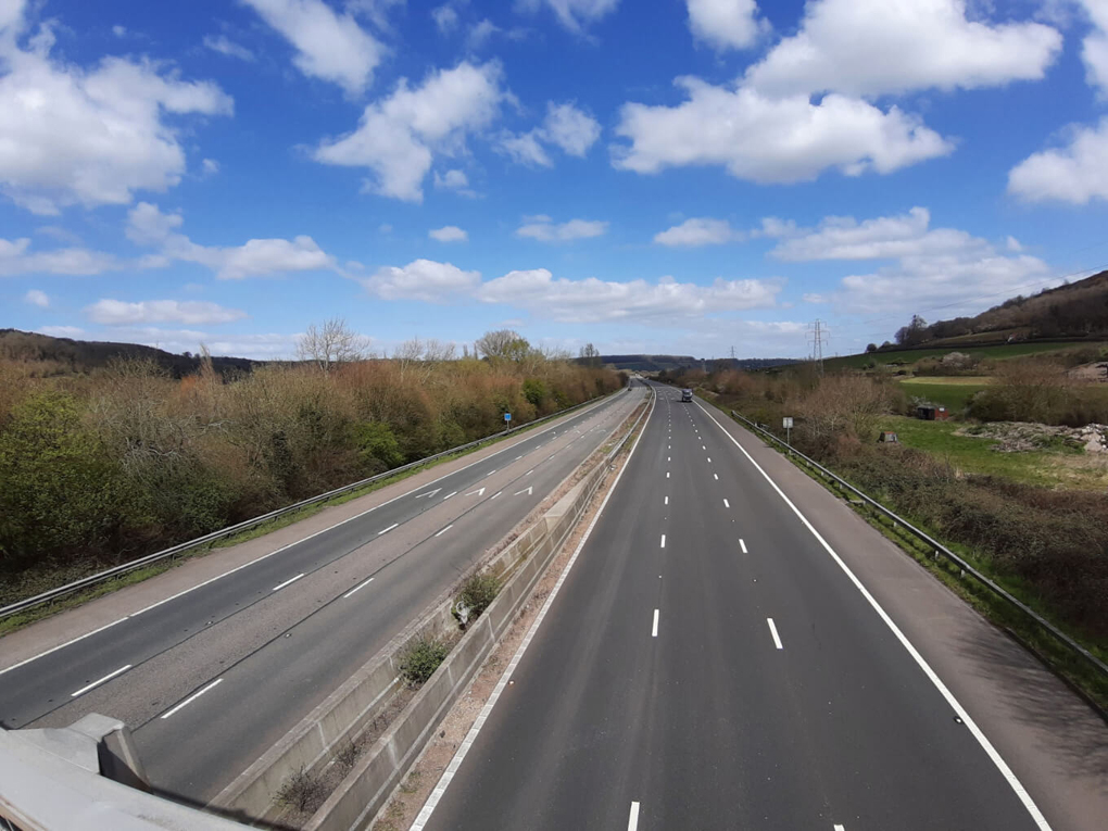 View of an English motorway banked by green hills on either side, with almost no traffic using it during the British COVID-19 lockdown in late March 2020