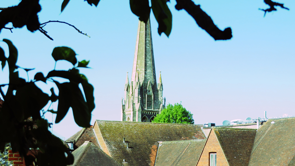 The spire of St Martin's church Dorking  is framed by rooftops on a sunny lock-down day.