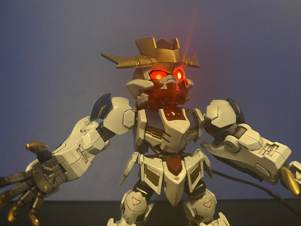 A Super Deformed Cross Silhouette Gundam Barbatos Lupus Rex, with custom paint job giving it deep reds, dark blues, gold claws, and LEDs lighting the eyes. The LEDs cause lens flare, making it look menacing.