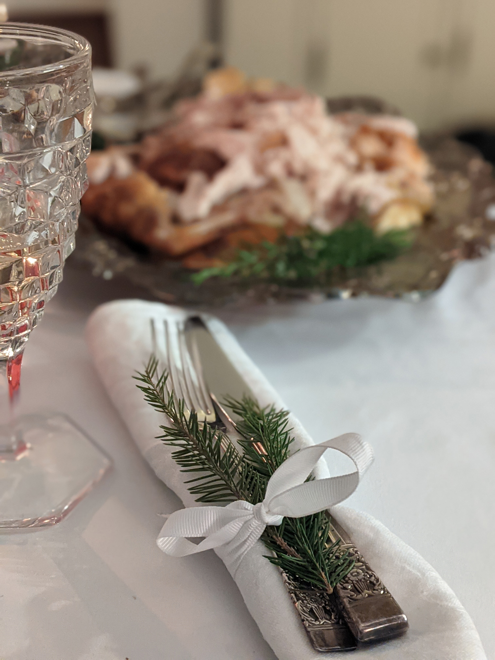 Cutlery wrapped in napkin with festive foliage, blurred platter of turkey in background