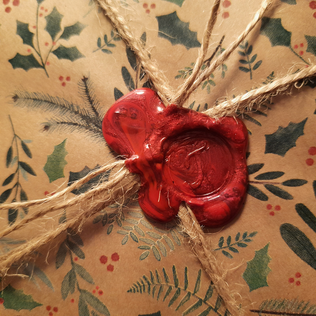 A red wax seal with a letter J stamped onto Christmas wrapping paper