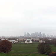 Photograph overlooking the historic buildings and university in Greenwich with London shrouded by fog in the distance.