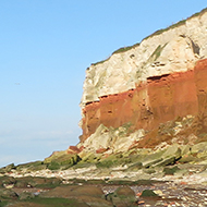 the red and white cliffs of Hunstanton, with a blue sky frame the beach which is covered in large boulders.