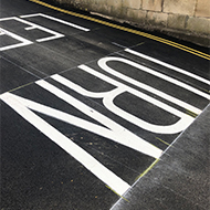 The words 'Turn left' painted in large white letters on a black road