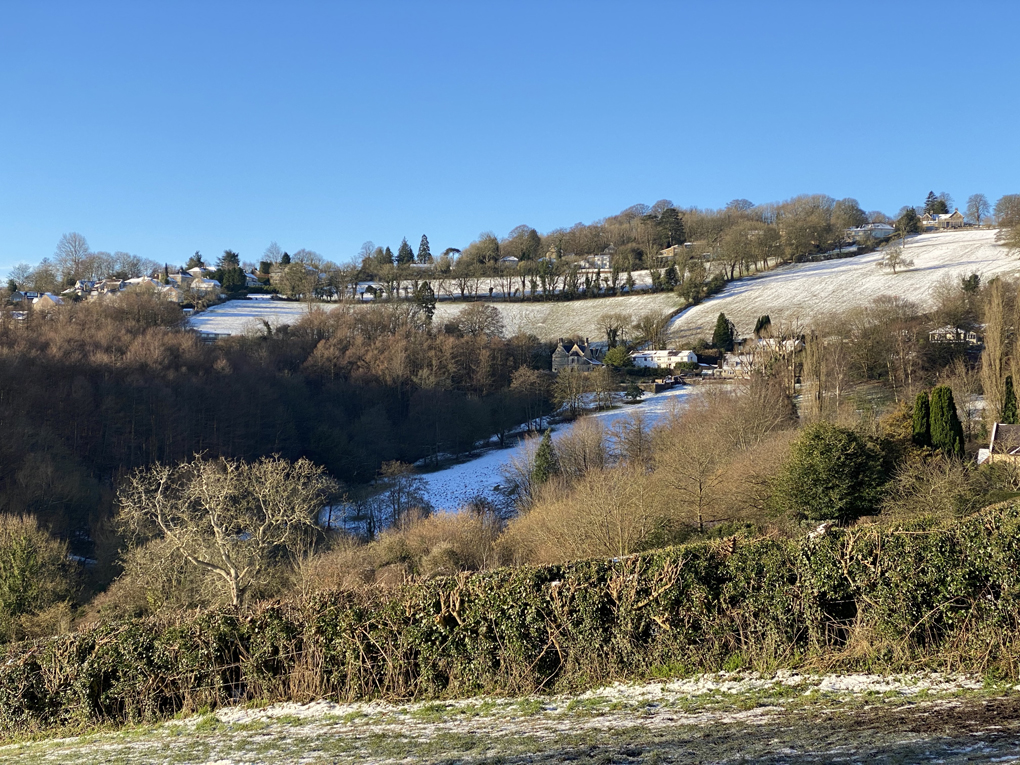 A view of hills, fields and trees, all lightly dusted with snow, under a clear sky