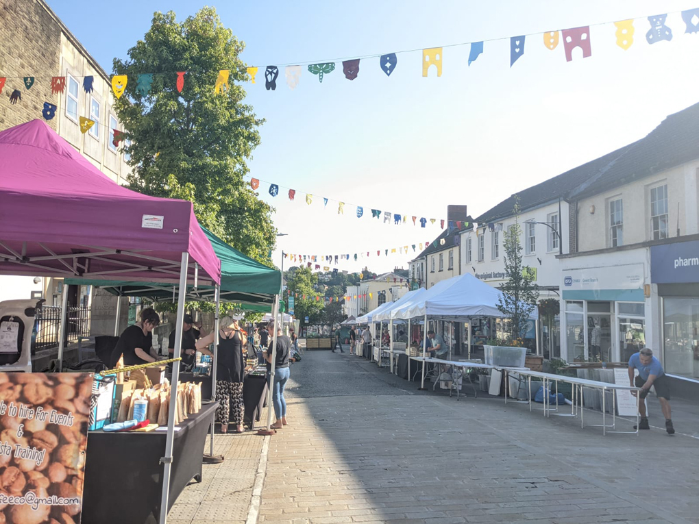 A quiet town street with stalls being set up, bunting overhead and and sunshine making things look cherry and colourful.