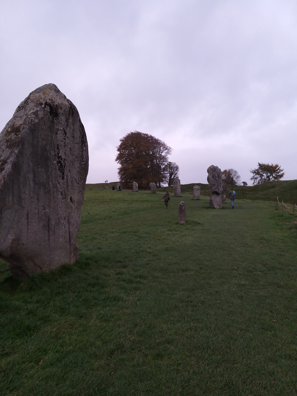 A section of the Avebury stone circle framed by green grass and a cloudy sky.