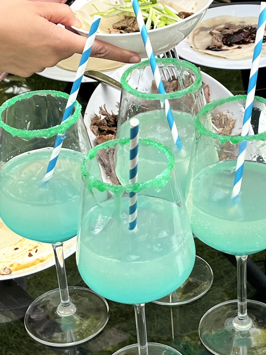 Four palmoas in cocktail glasses in front of some food.