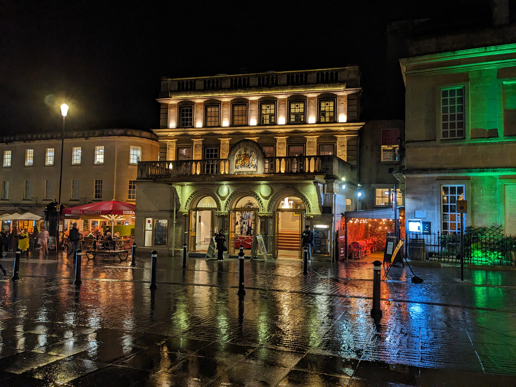 The Theatre Royal at night in the rain with lights shining different colours reflecting in the water