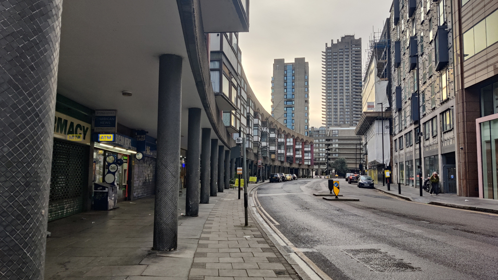 A grey day walking through Barbican past the colonnade of shops with tower blocks above