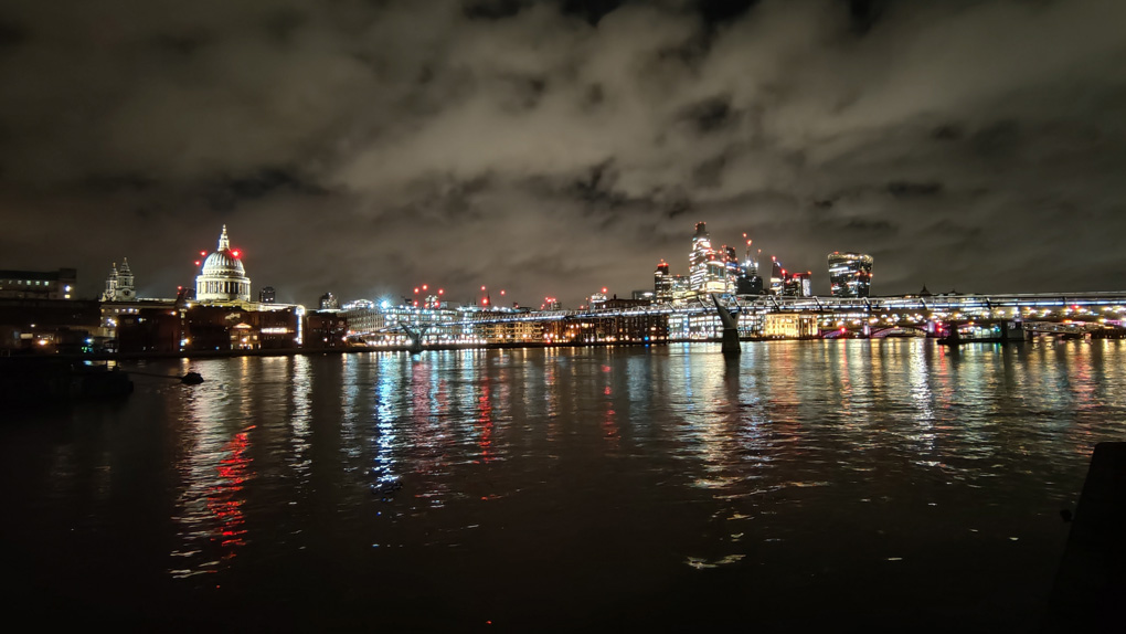 The city of London skyline at night is a forest of lights which reflect in the Thames by the Millennium footbridge.