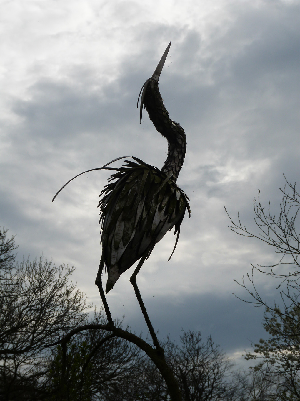 An ironwork sculpture of a heron (I think!) balances precariously against a bright sky.