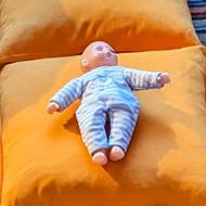 Baby doll on a cushion surrounded by other plush toys