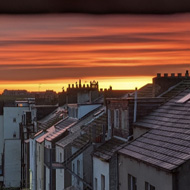 View of alleyway and rooftops. Whitby Abbey in the background shadowed against an orange and golden sunrise