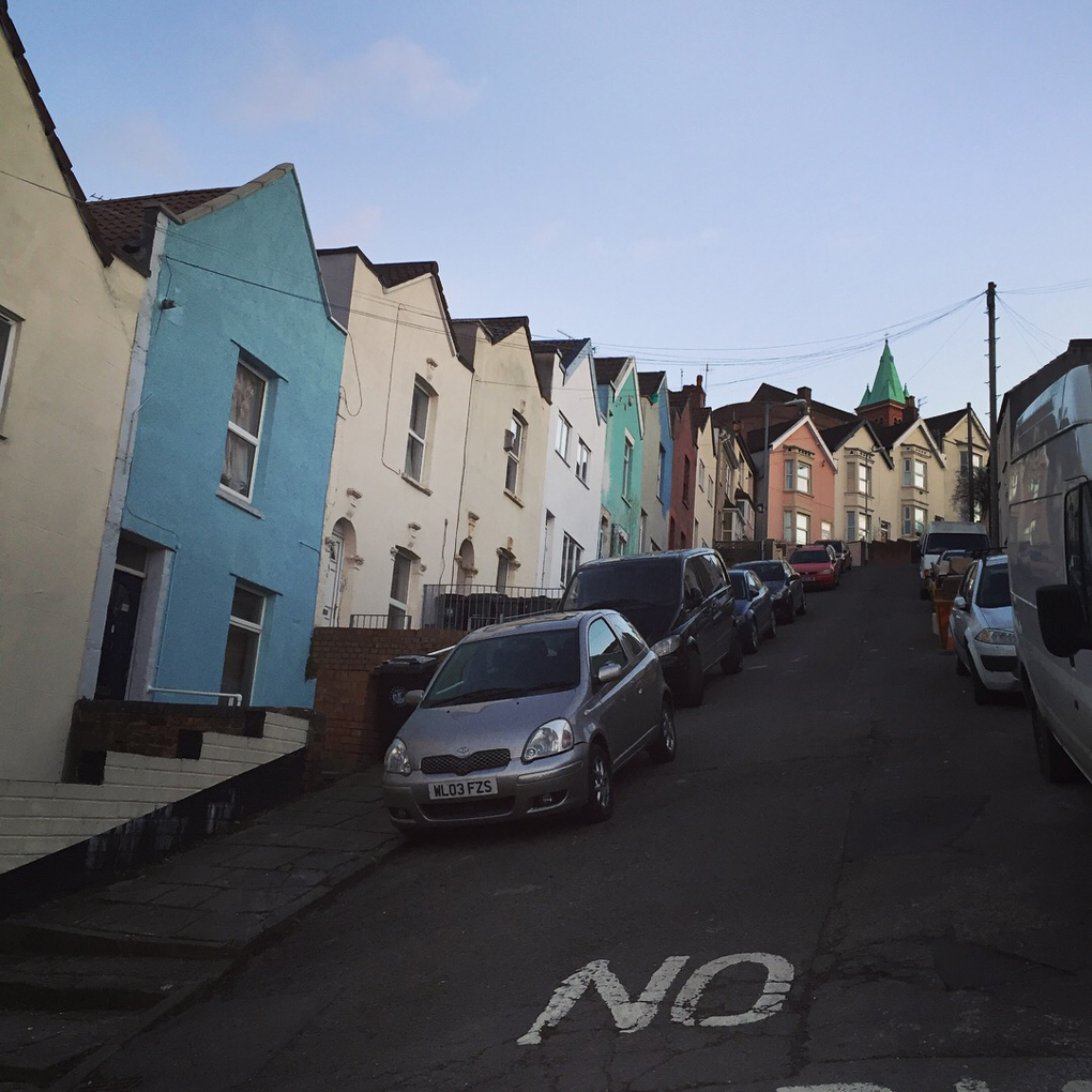 A very steep residential street with parked cars at an angle. Signage on the asphalt reads 'NO'.