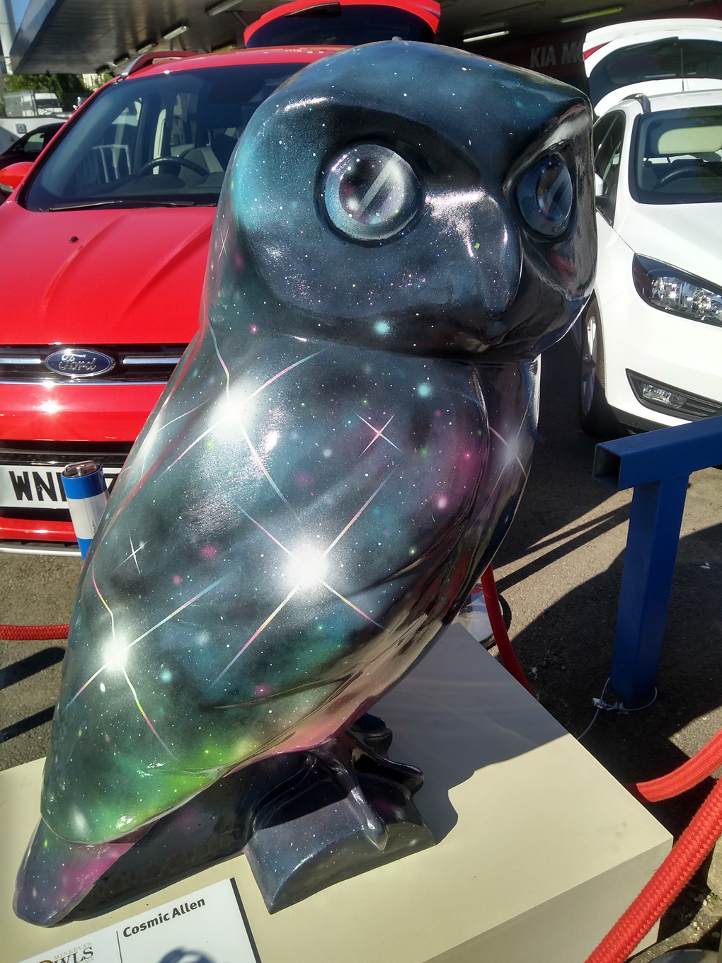 A giant model of an owl painted with the cosmos in a car dealership forecourt.