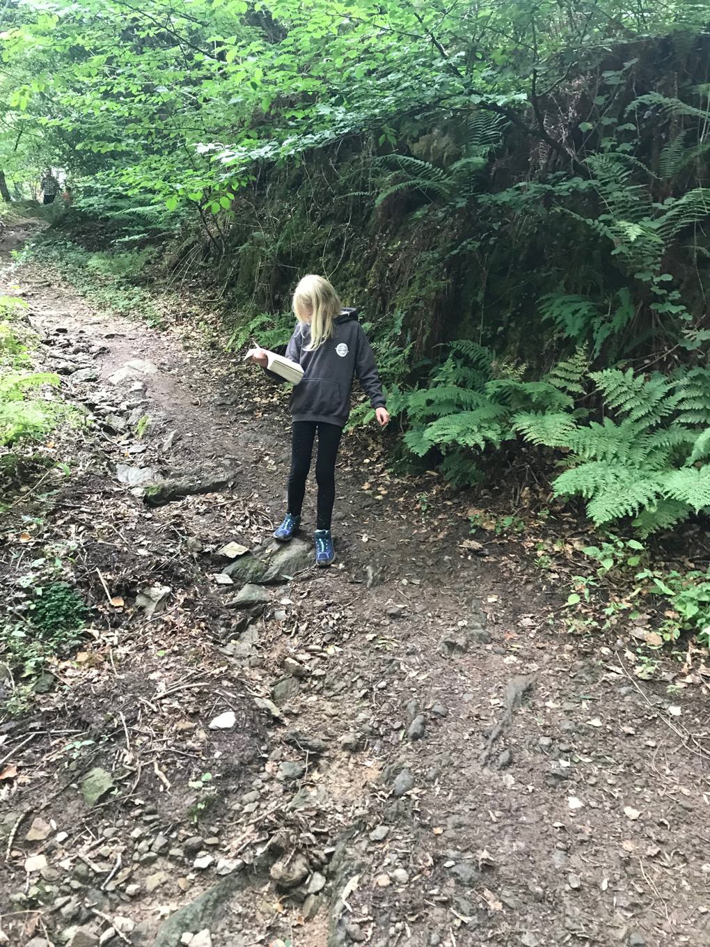 girl reading a book while walking through a wood