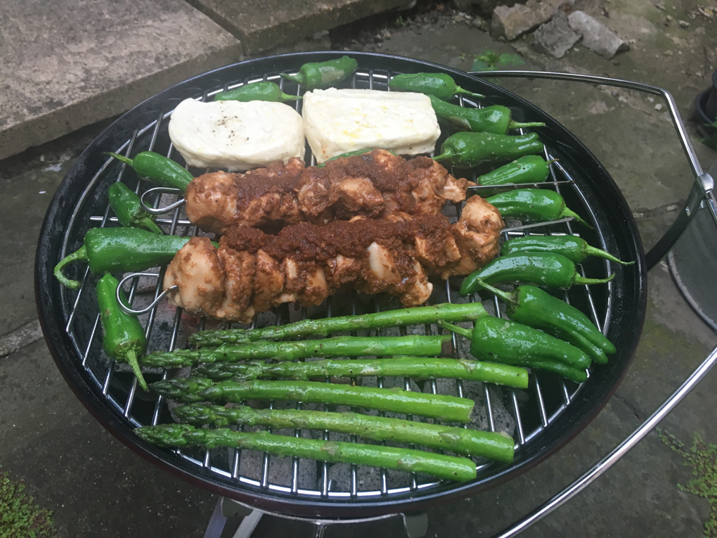 Chicken with homemade adobo, asparagus, and padron peppers on a barbecue.