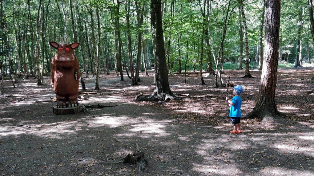 A small boy stands in a woodland area, near a carved statue of the Gruffalo.