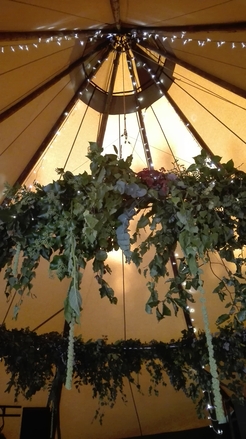 A circle of pretty foliage hangs in the peak of a yurt tent. The picture is taken from below.