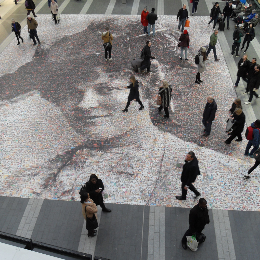 A picture of a womans face, members of the public are walking across it