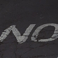 A very steep residential street with parked cars at an angle. Signage on the asphalt reads 'NO'.