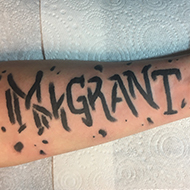 The inside of Sean's left forearm with a fresh tattoo that reads 'immigrant'