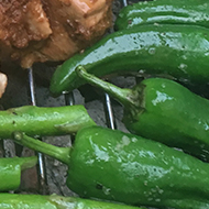 Chicken with homemade adobo, asparagus, and padron peppers on a barbecue.