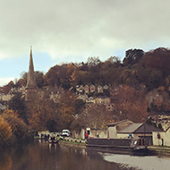 View of the canal and the towpath, with autumnal trees and houses on a hillside in the background