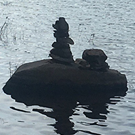Rocks carefully piled to create a tower on the shore of a quiet lake
