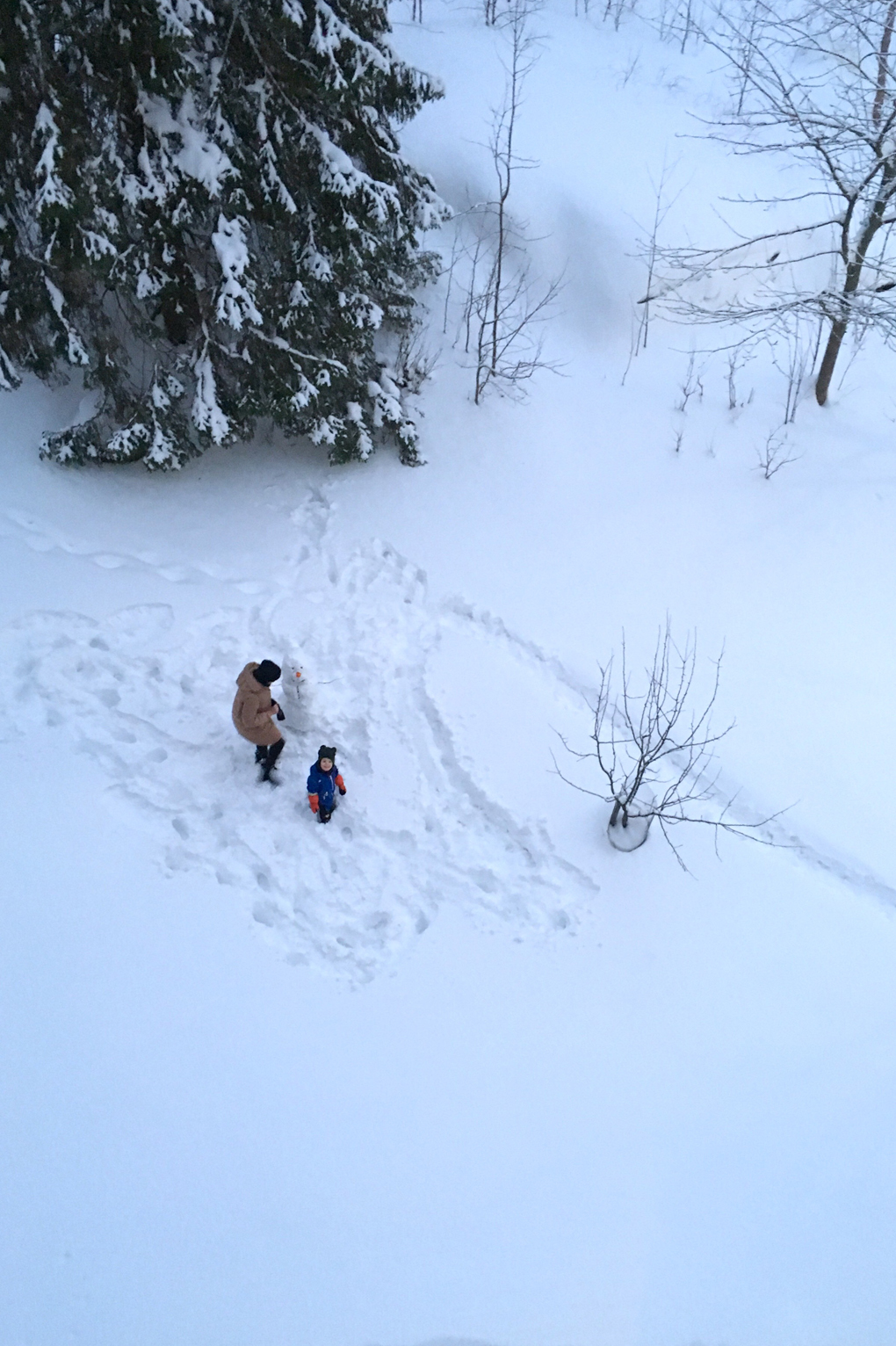 Aerial view of an adult and a child building a snowman