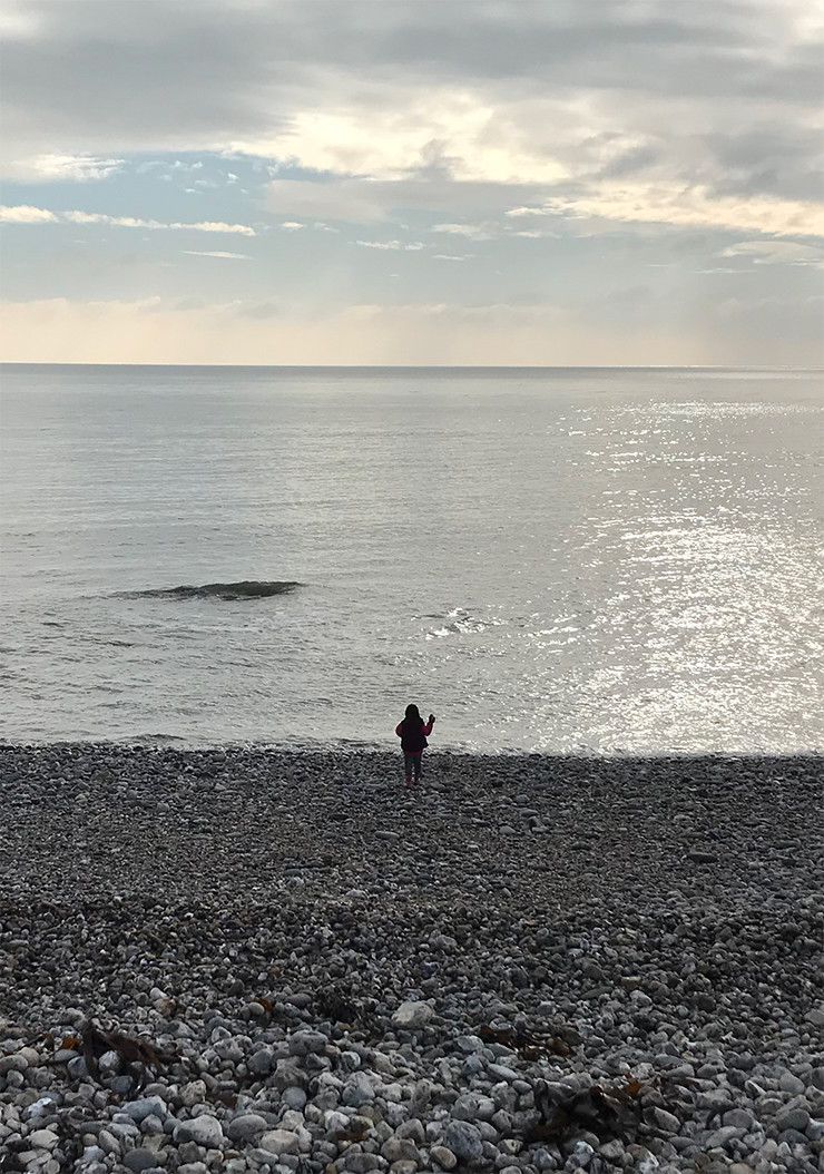 Small human throws stones into big ocean