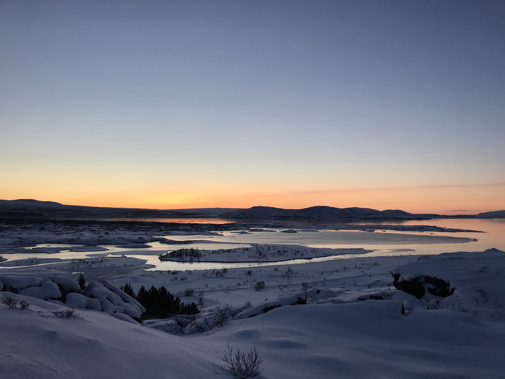 Sunrise over a flat landscape of snow and lakes with small mountains in the distance