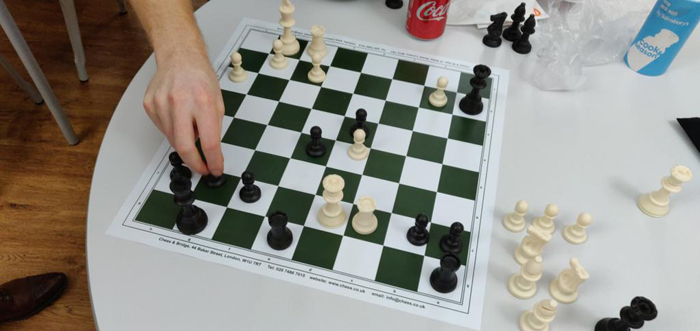 A chess game in its late stage viewed from above. The board is on a table in an office lunch area.