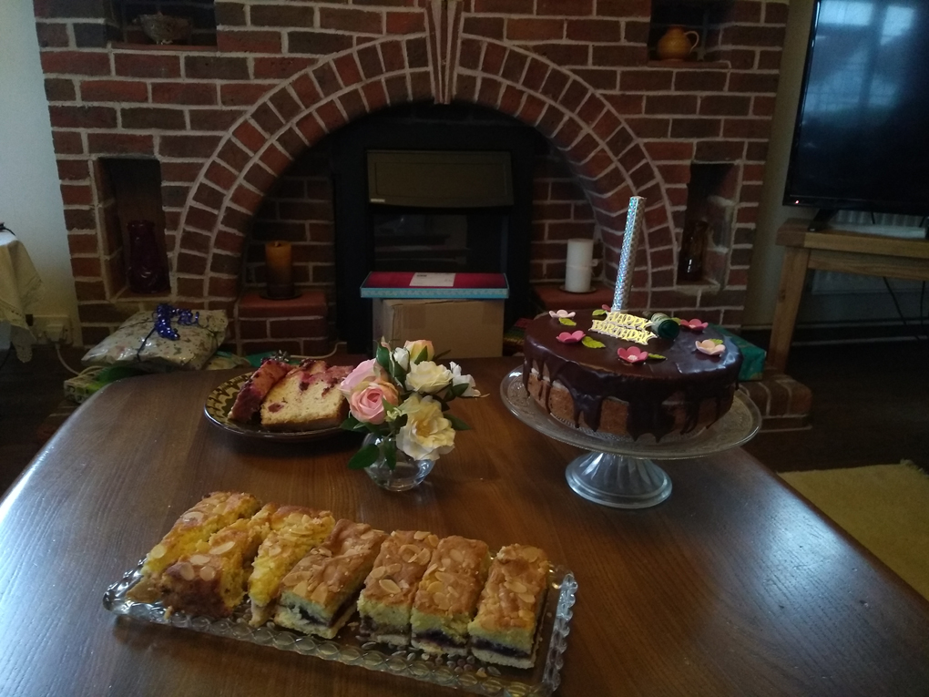 Table in front of fireplace with cakes on top, including birthday cake with unlit firework type candle