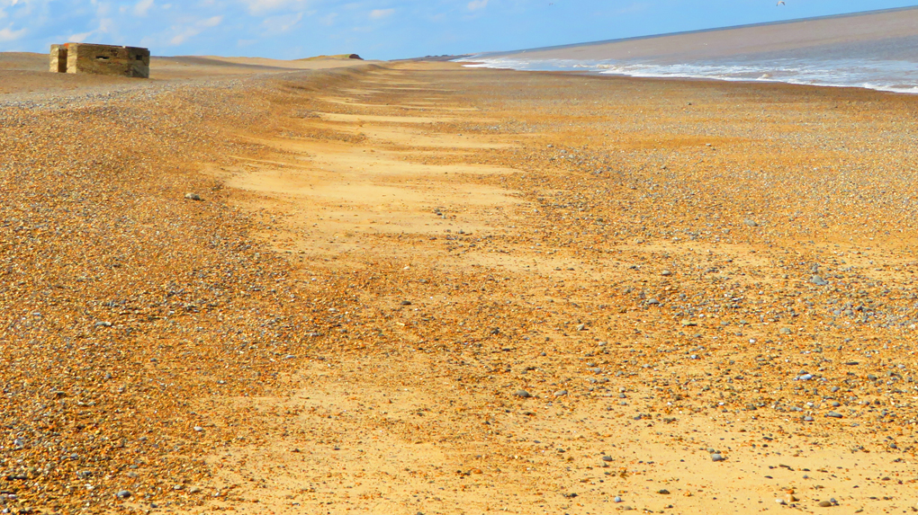 Pill box on a deserted shingle beach moving slowly into the sea.