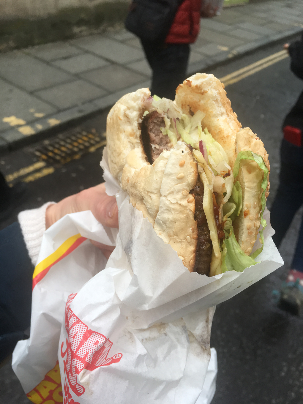 A hand holding a burger with a piece bitten off.
