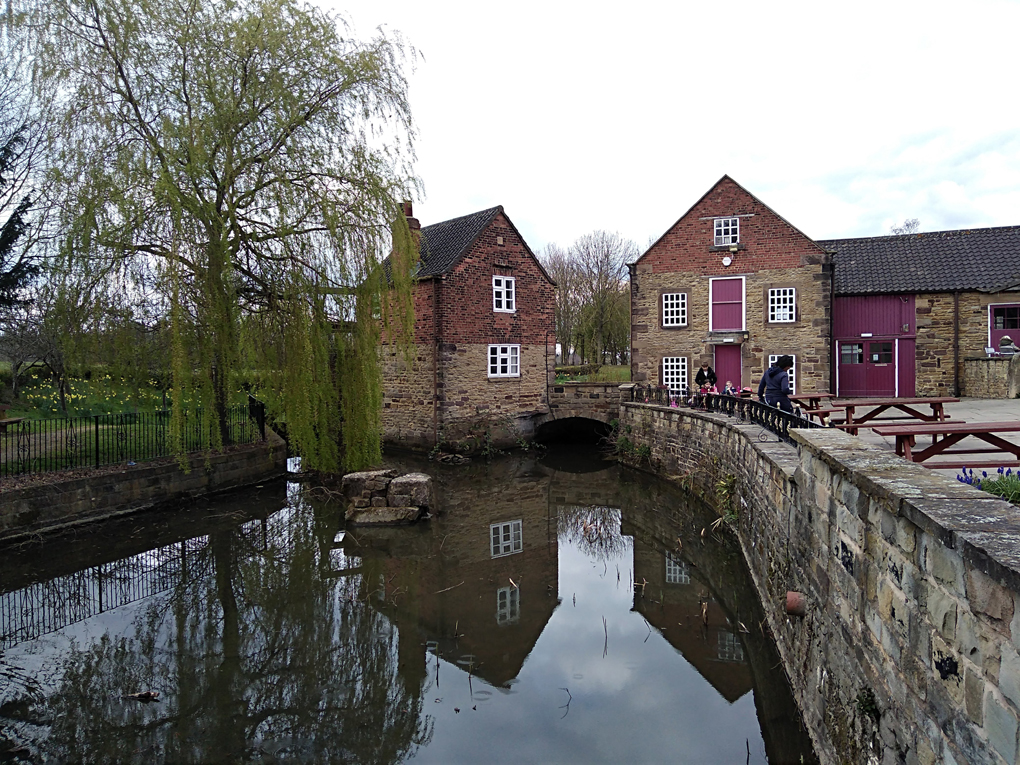 This picture shows a mill house and willow tree which are beautifully reflected in a pond