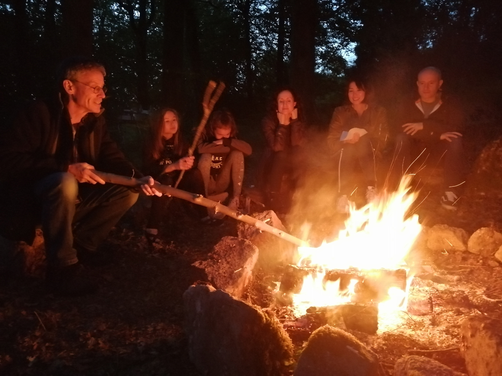 Family gathered at dusk around a fire. Jon has large poking stick.