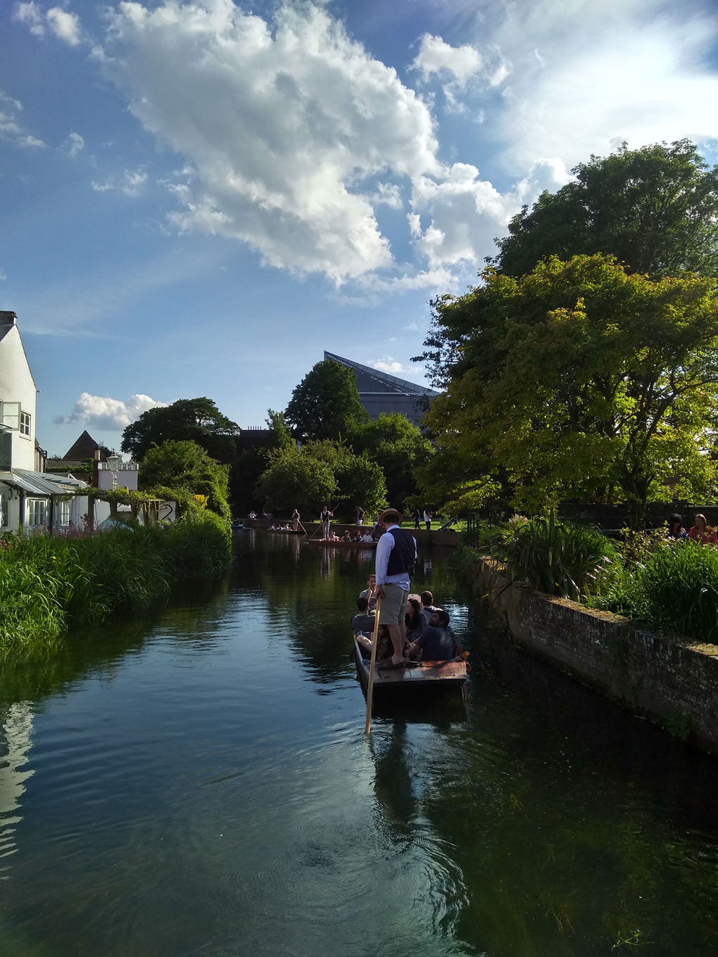 Punting boats on the river Stour in Canterbury by a park with Marlowe Theater in the background.