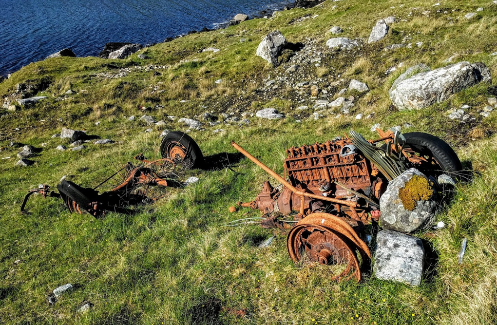 Rusted car on a slope between road and loch in the Outer Hebrides.
