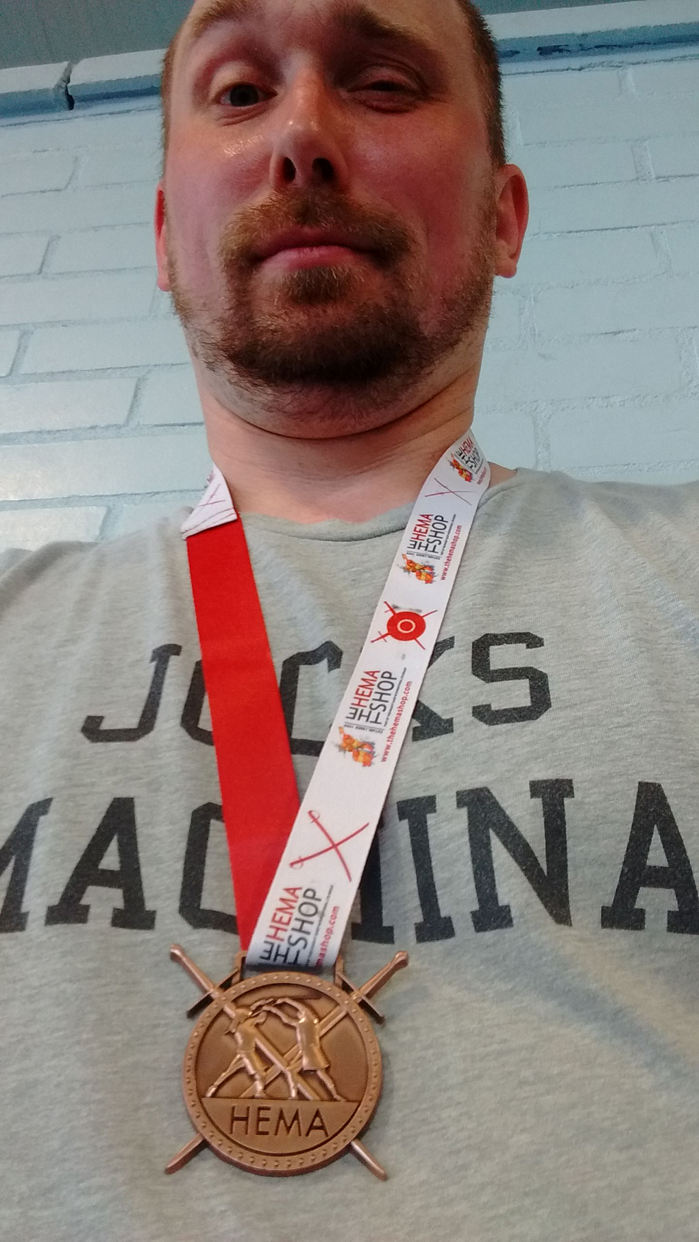 A slightly red-faced, balding man raises his eyebrow in this selfie whilst wearing a bronze medal