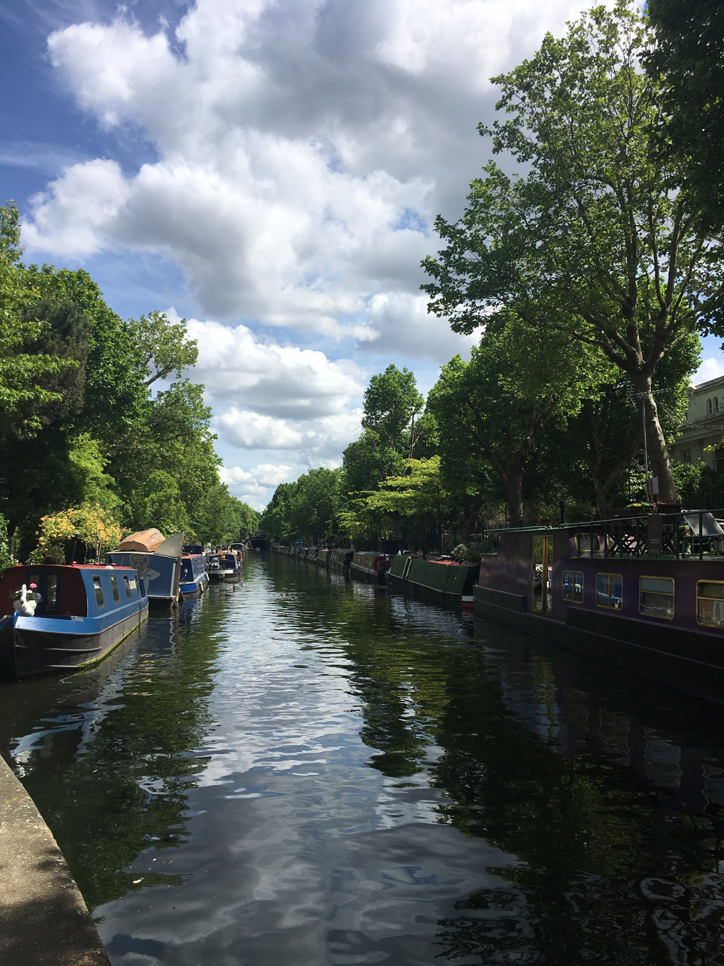 Avon and Kennet canal stretching into the distance with narrow boats moored to either side and sunlight shining off of emerald water