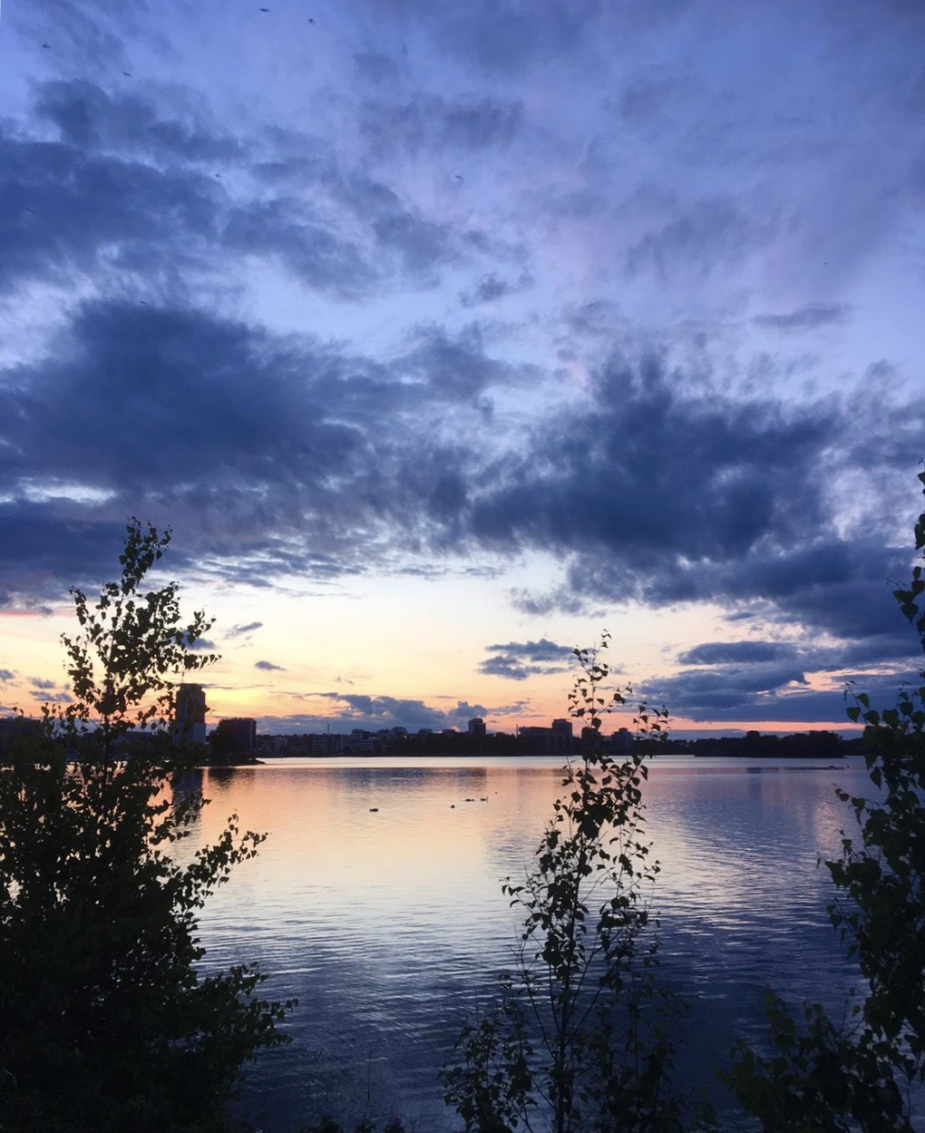 Sun setting over water with a silhouette of buildings in the distance.