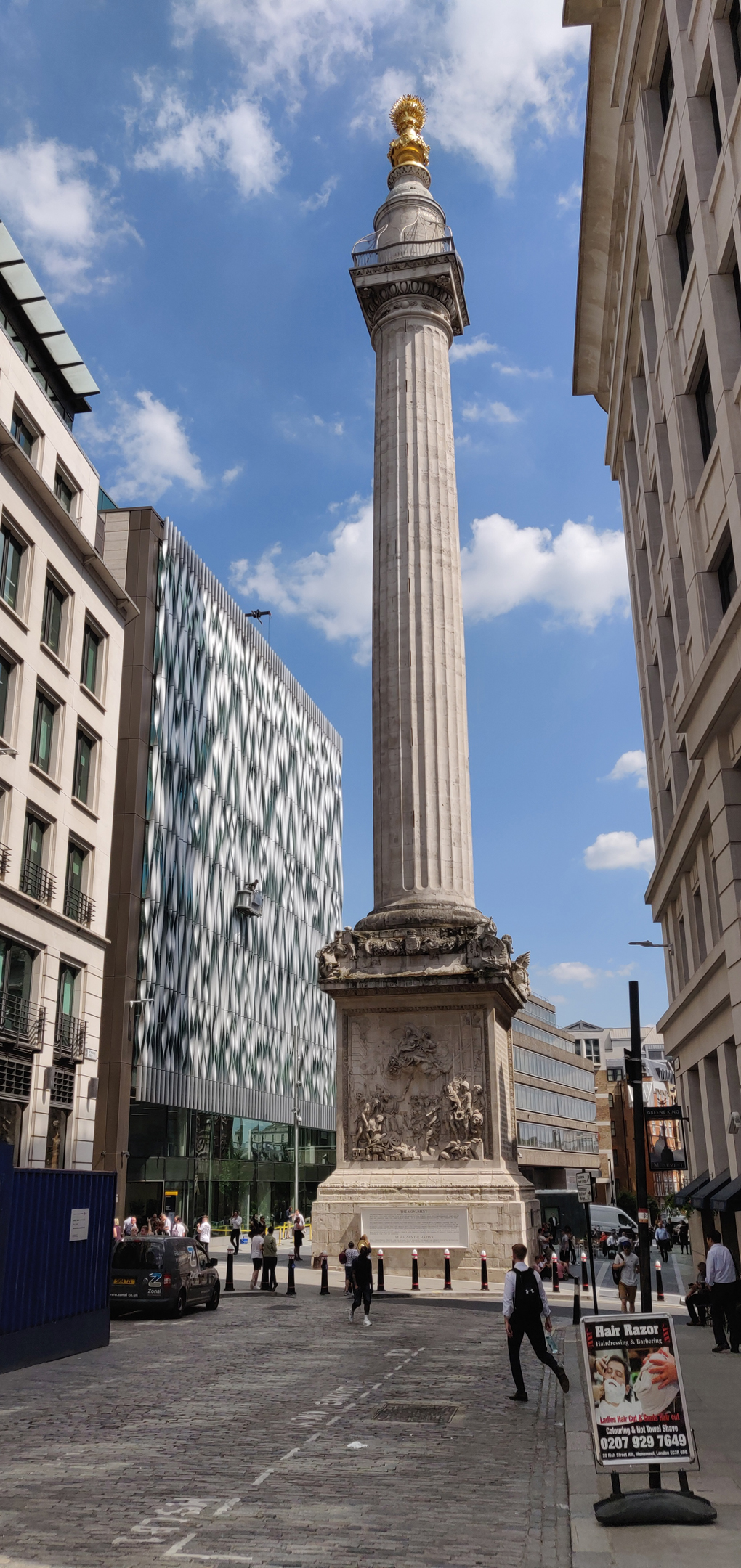 The Monument to the Great Fire of London rises above narrow London streets with its golden urn high up catching the sunlight.